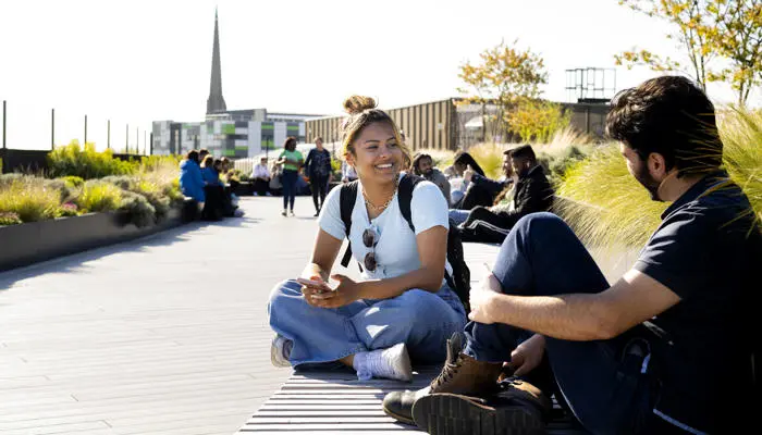 group of students sat in the student centre rooftop garden with a church spire in the background