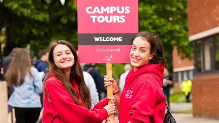 Two student ambassadors holding a campus tours sign.