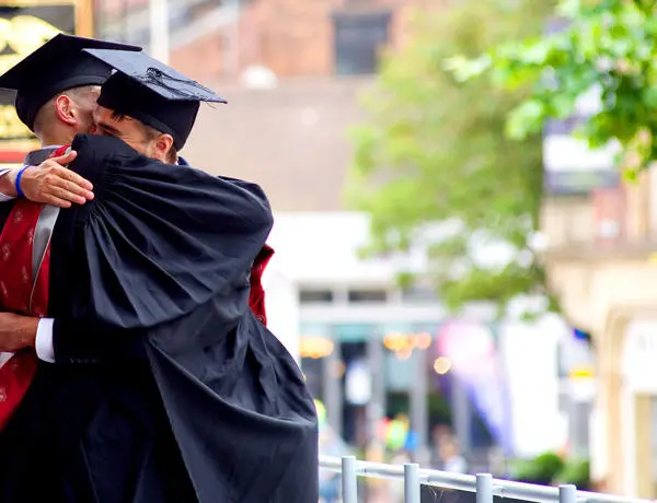 Graduates hugging in graduation gown and hat