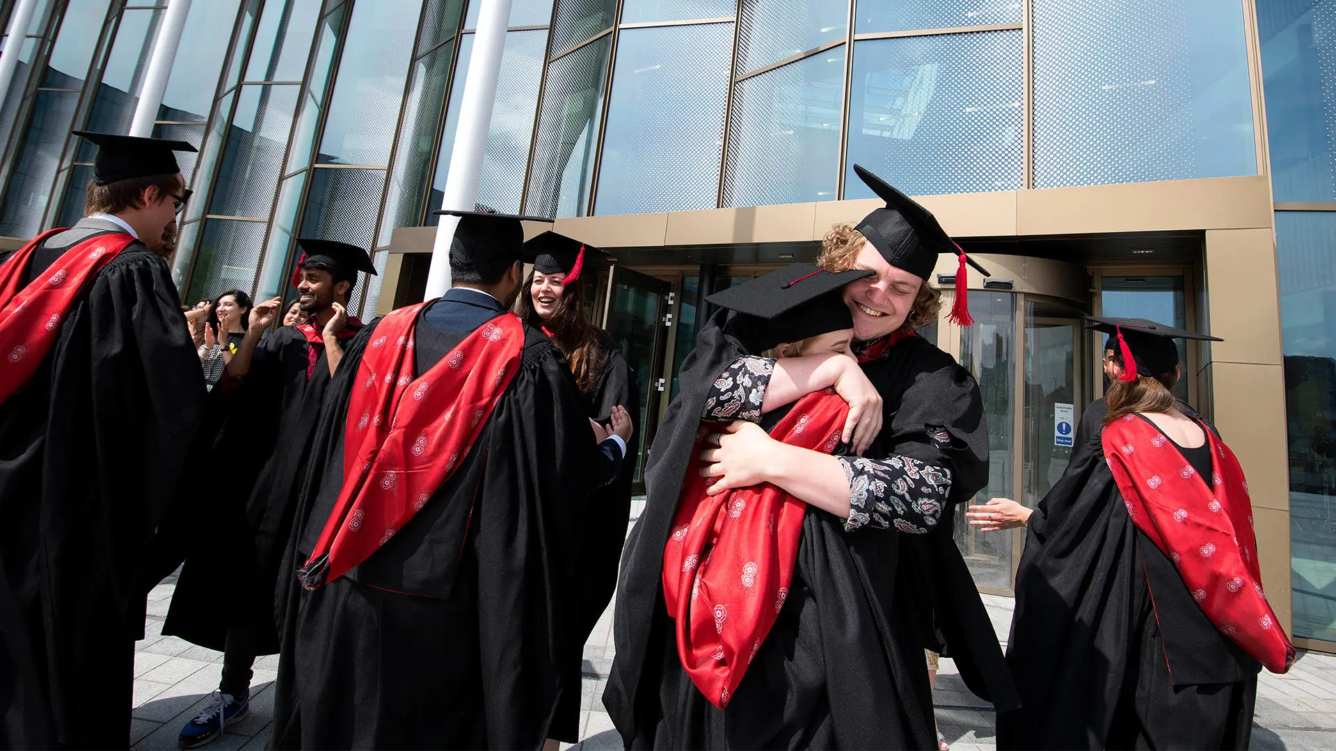 Students in graduation gowns embracing outside the Student Centre building