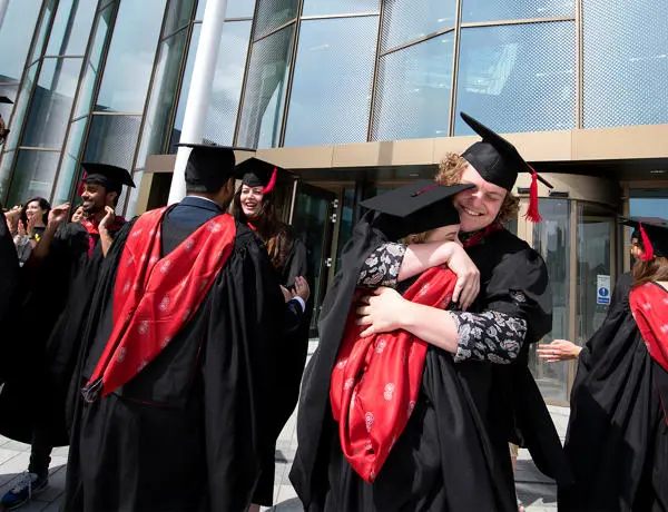 Students in graduation gowns embracing outside the Student Centre building