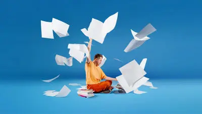 Accounting and Finance student sat cross legged in front of a laptop surrounded by books and sheets of paper in the air