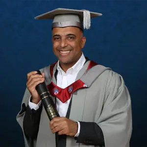 Zuber Issa dressed in graduation gown holding an Honorary Fellow award