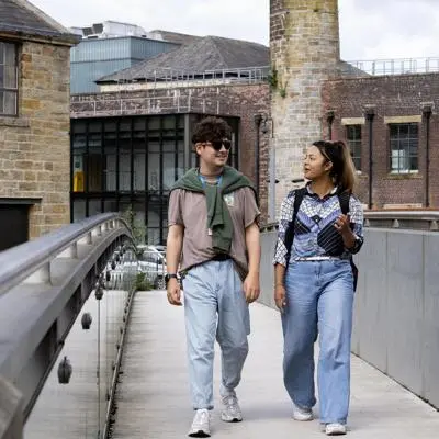Two students walk along Sandygate bridge talking to eachother.