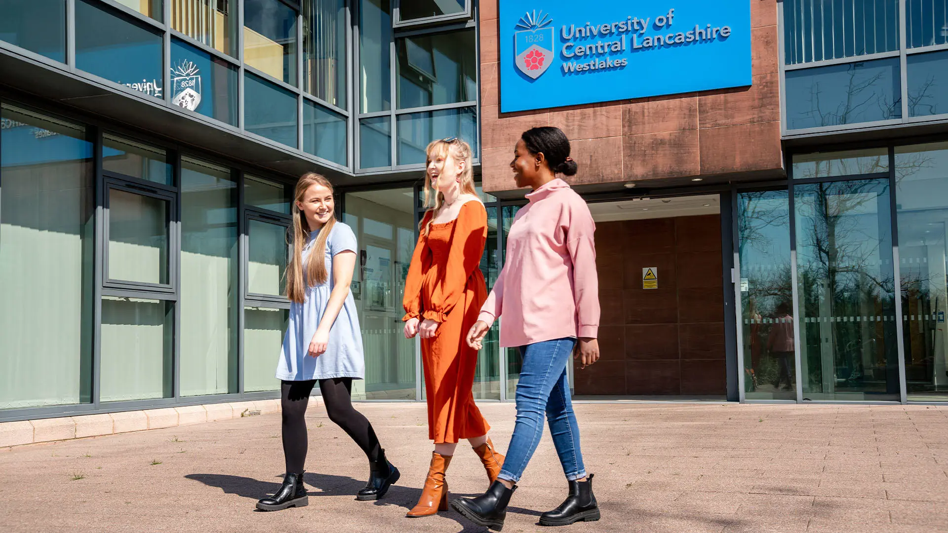 Three students walking on Westlakes Campus in the sun