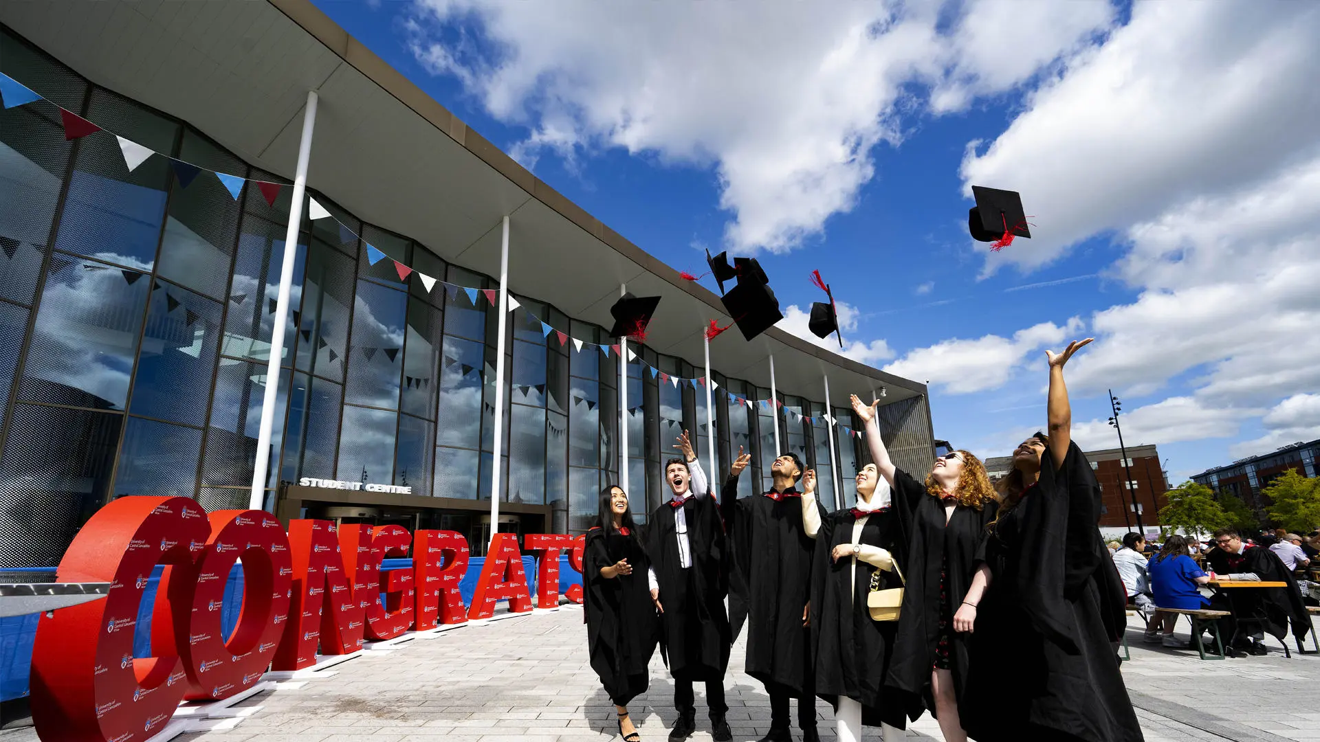 group of graduation students throwing their caps in the air next to a congratulations sign outside the student centre