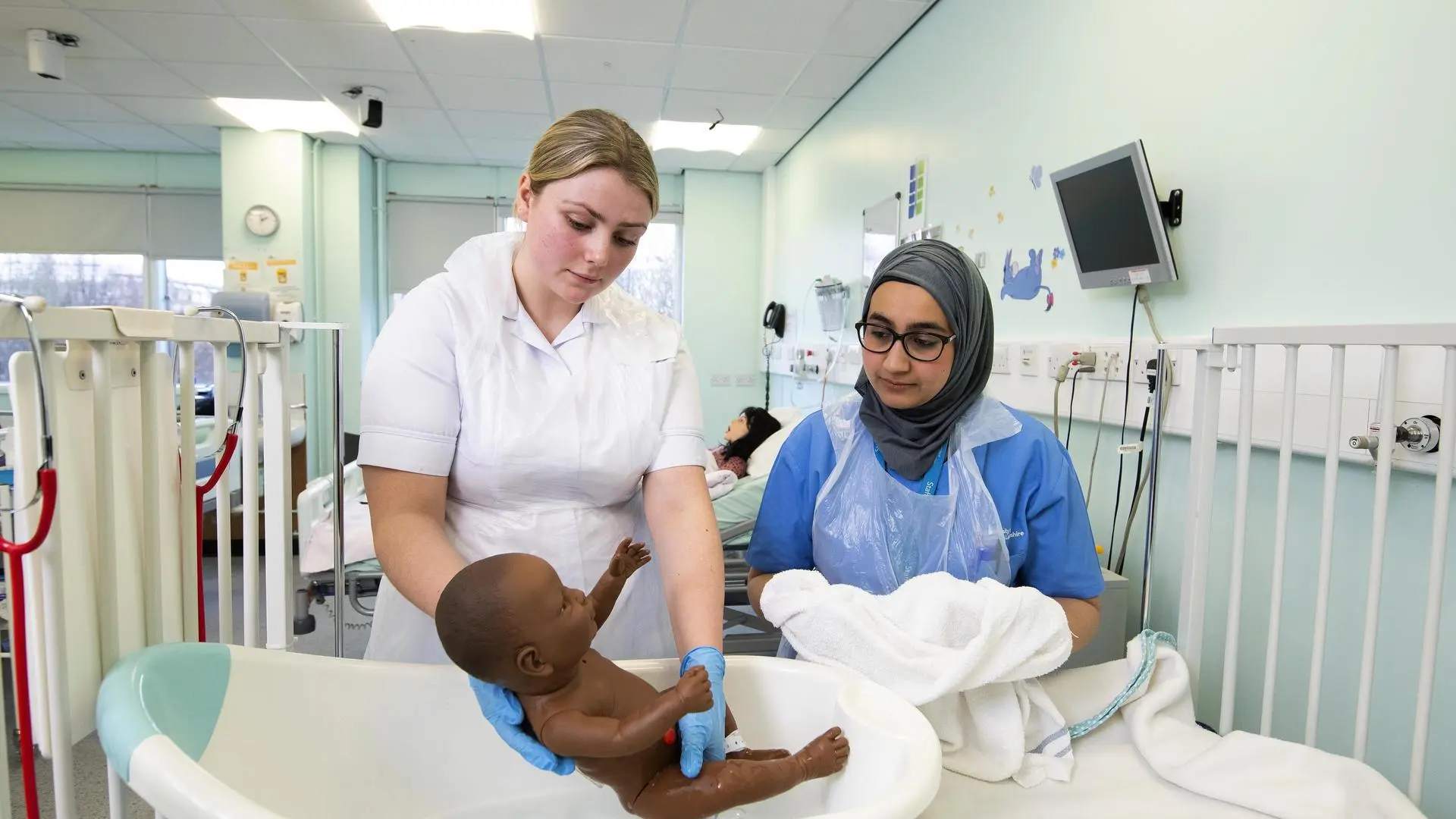 Two students hold a baby manikin in a midwife ward simulation suite.