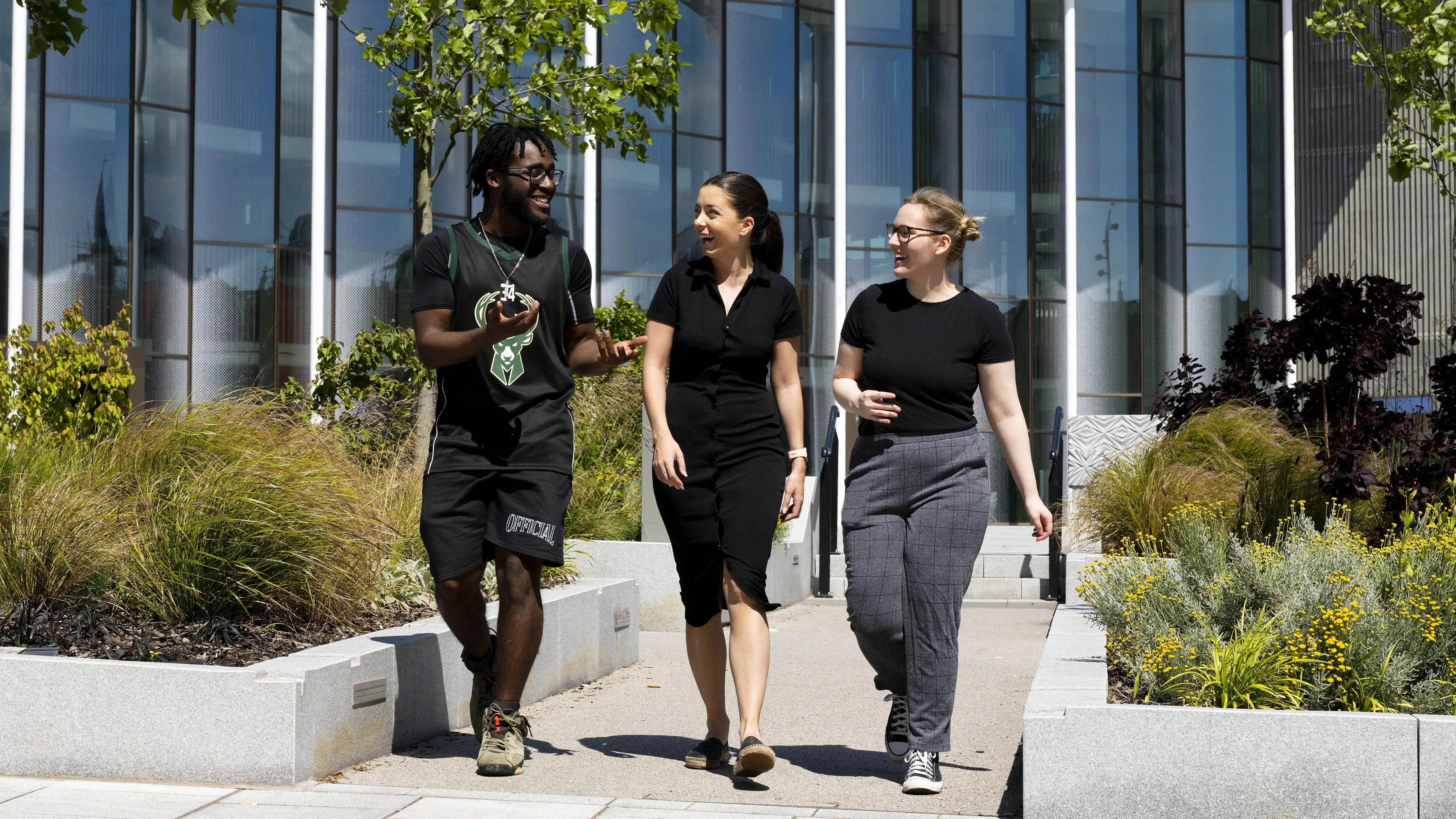 Three students talk to one another, whilst walking through Preston campus on a sunny day