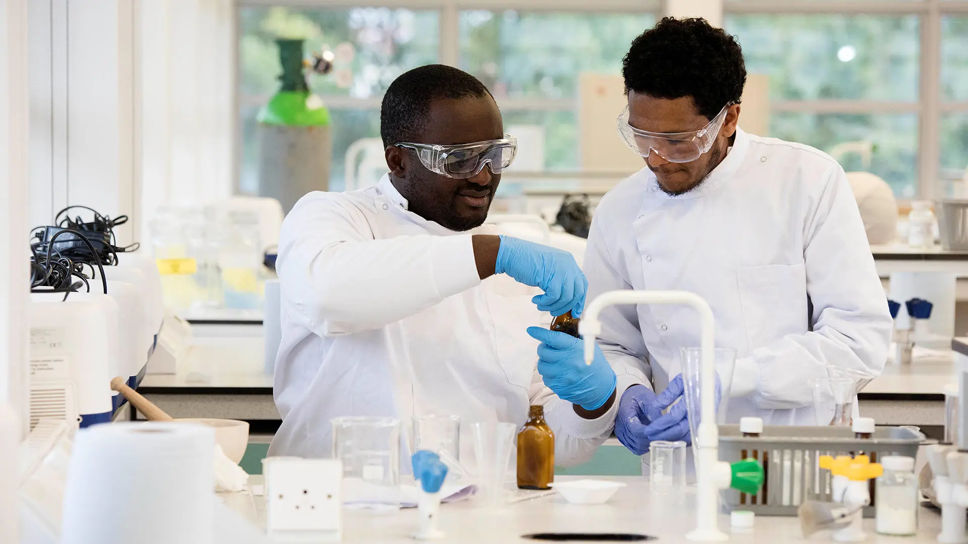 Students dressed in lab coats, goggles and gloves working together in the laboratory