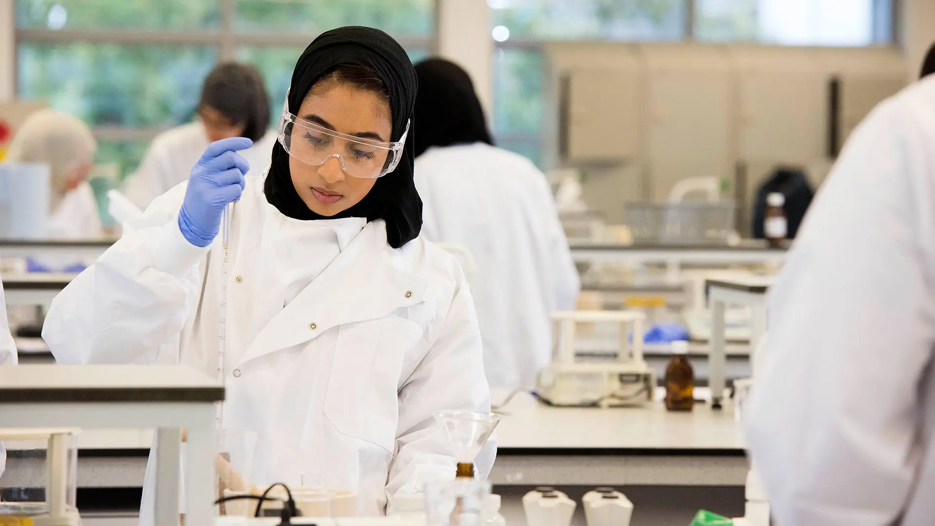 Student dressed in lab coat, goggles and gloves working in the laboratory