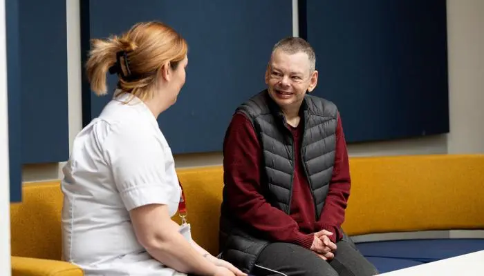 A nurse sat talking to a male patient who smiles in response