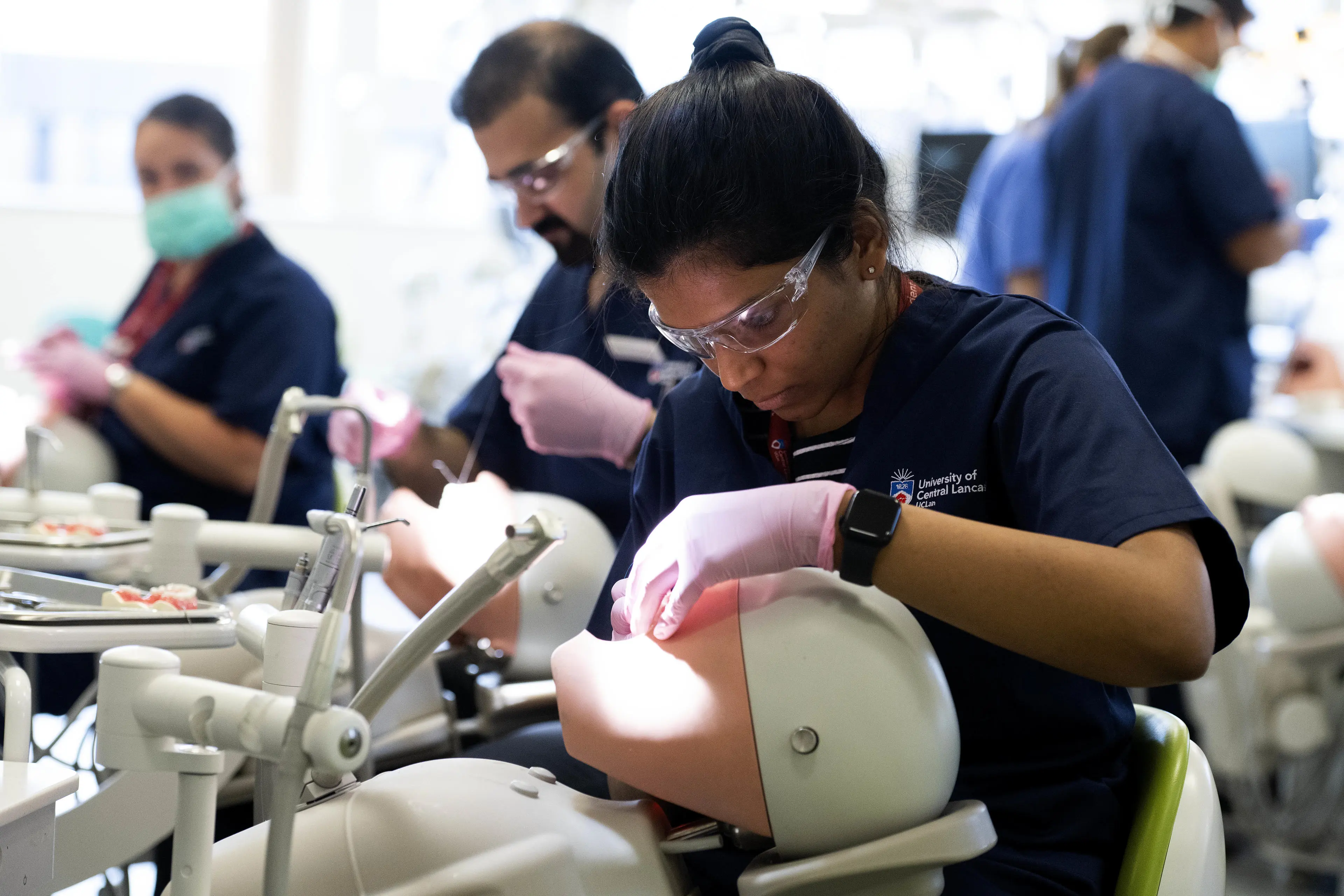 A dental student works on a dummy with other students also seen working in the background