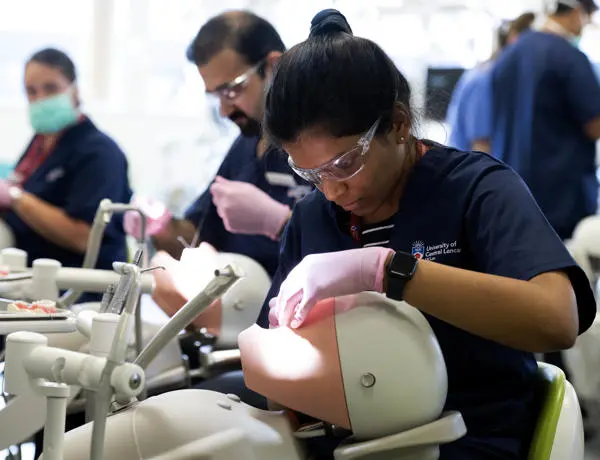 A dental student works on a dummy with other students also seen working in the background