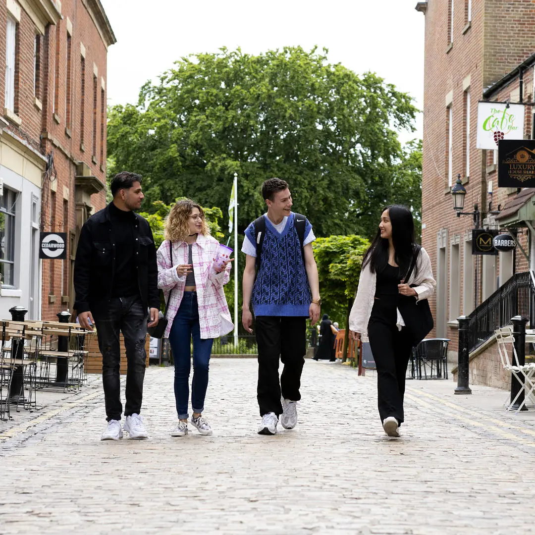 group of students walking along winckley street past bars and restaurants, winckley square in the background