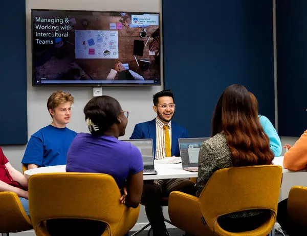 International Business students talking part in a discussion around a table with screen in background