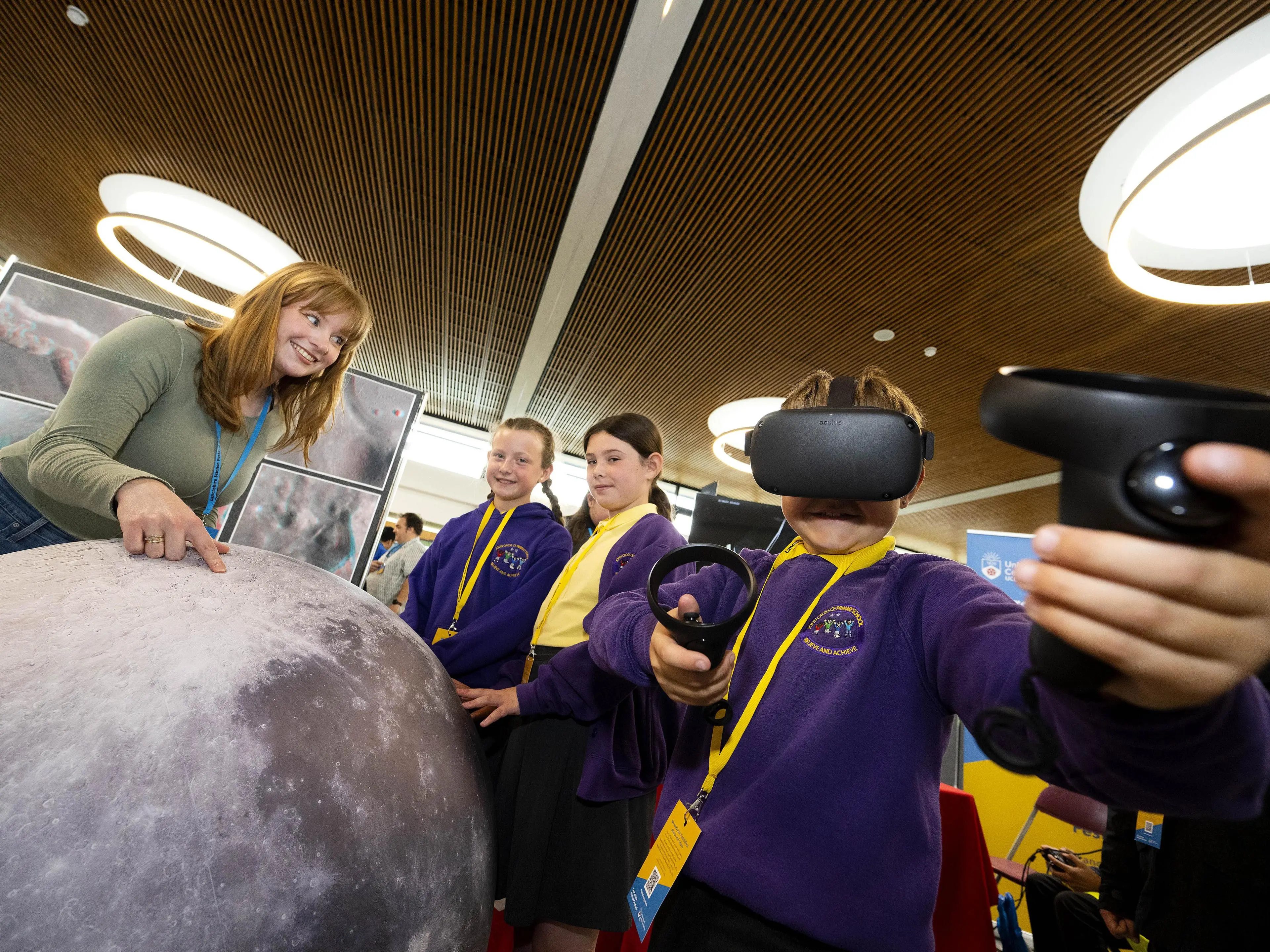 Primary school students wear VR headsets next to a model of the moon.