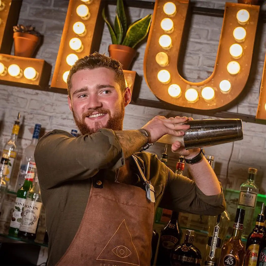 Bar staff member shaking cocktail in apron at Illuminati Bar Burnley
