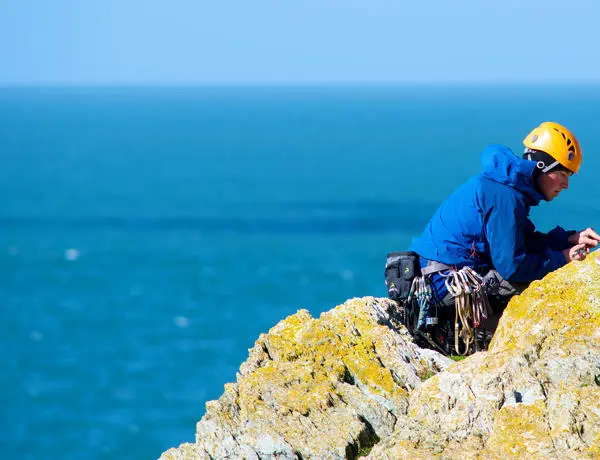 Mountain climber scaling a large rock beside the sea