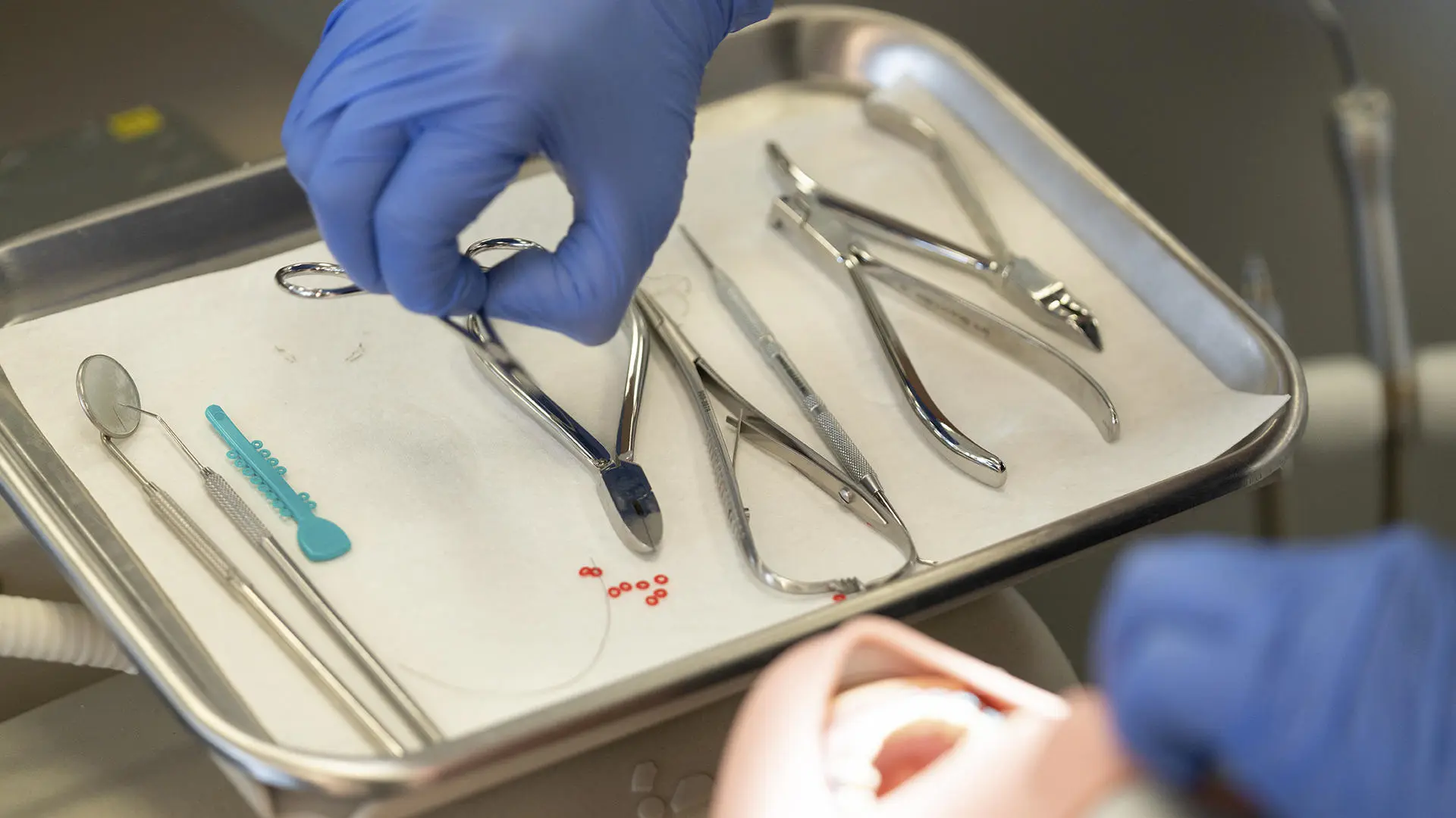A dentist picking up a dental tool from a tray populated with other dental tools