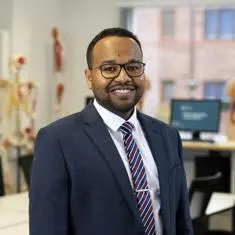 Asim in a blue suit and glasses smiling