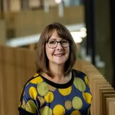 academic member of staff headshot stood in student centre wearing colourful spotty top