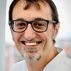 Flavio smiling in a white top and glasses