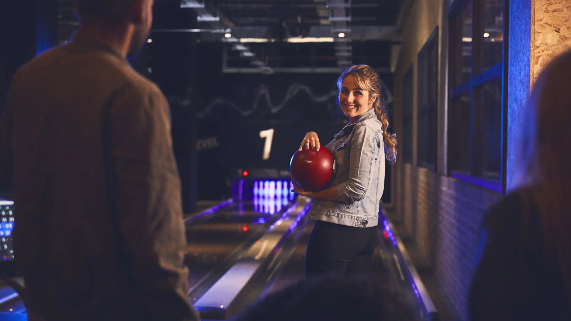 group of students in a bowling alley main focus of the email is a female student in a denim jacket holding a bowling ball