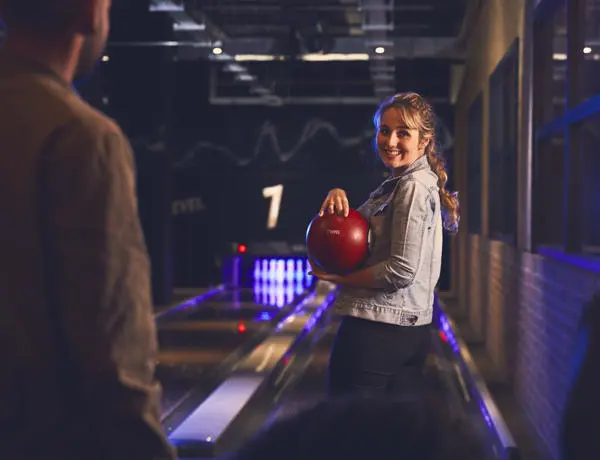group of students in a bowling alley main focus of the email is a female student in a denim jacket holding a bowling ball