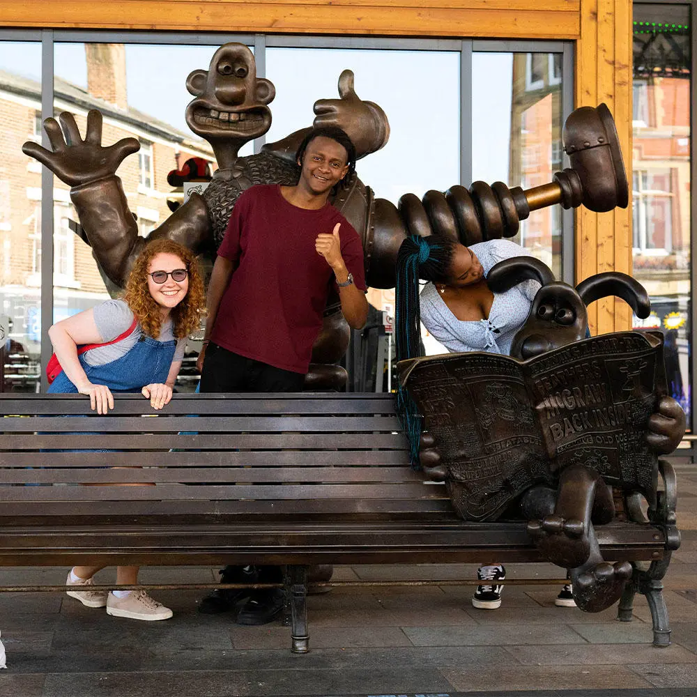 Three students posing with Wallace and Gromit statue outside Preston Market