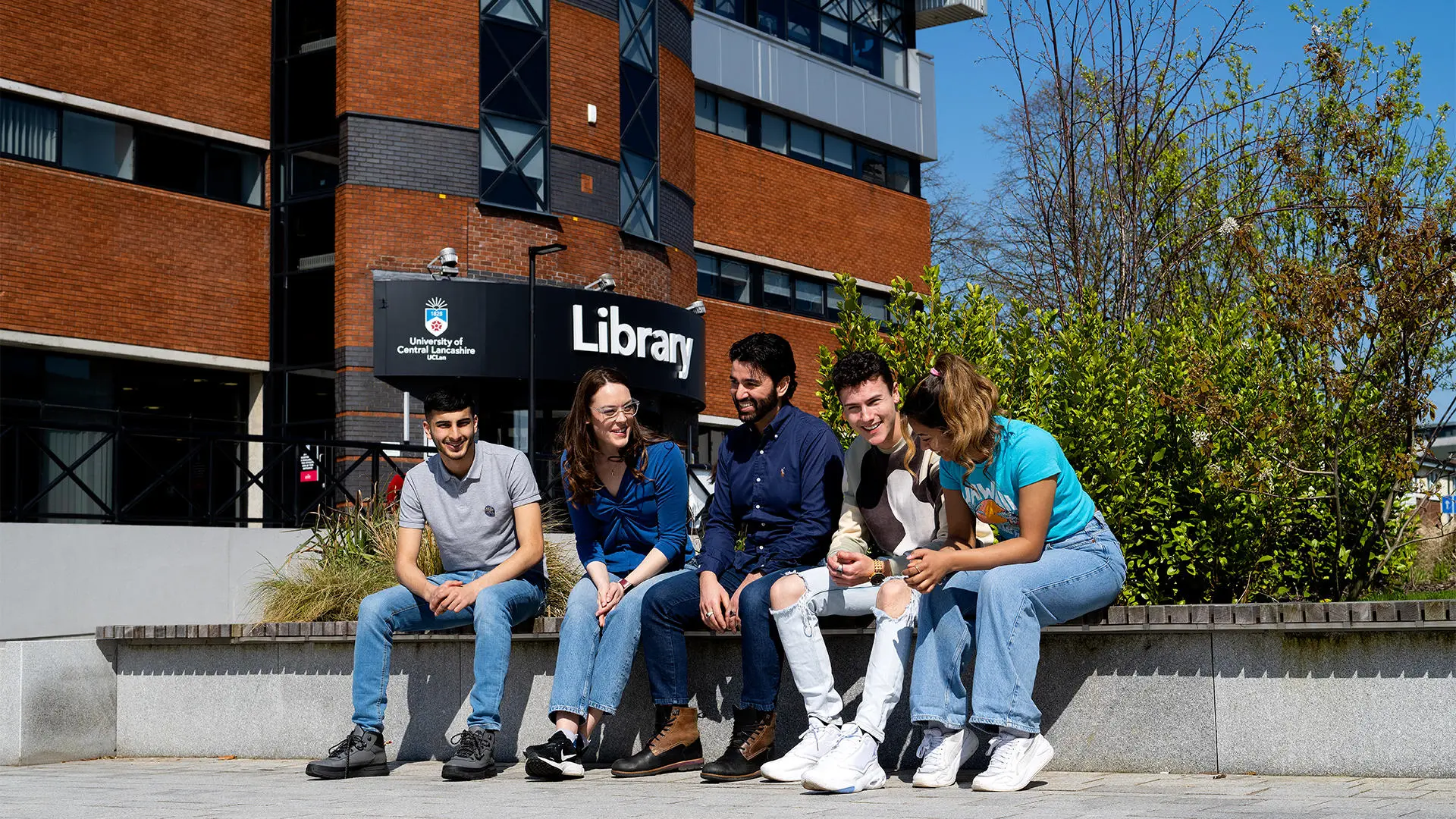 Group of students sat on bench near library talking
