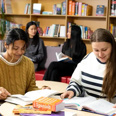Students sitting at a desk with language books and bookshelves in the background