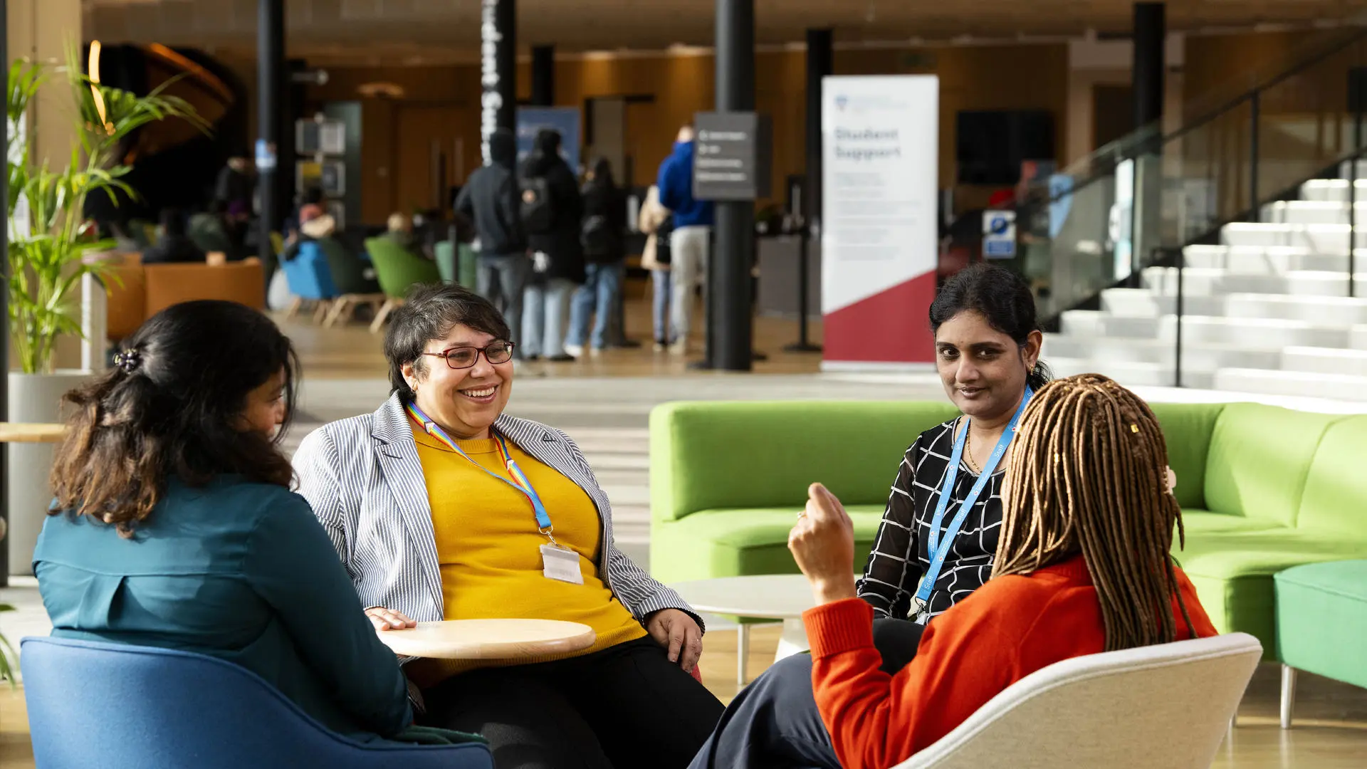 Group of UCLan staff sat chatting on sofas inside the student centre