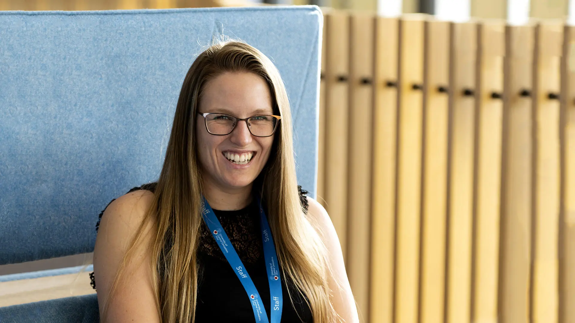 student coach Danielle Hunt wearing a black vest top, staff lanyard and sat at a table in the student centre smiling