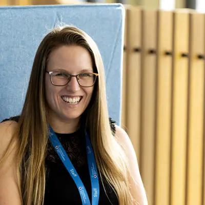 student coach Danielle Hunt wearing a black vest top, staff lanyard and sat at a table in the student centre smiling