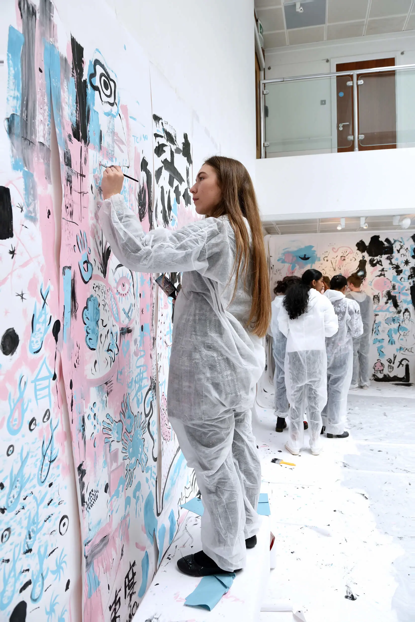 Young person in protective overalls painting on a wall as part of an arts workshop