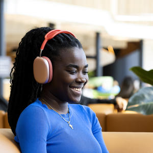 student sat on an orange sofa in the student centre looking at a laptop wearing headphones