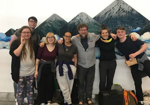Group of students with their arms around each other stood in front of a mountain range