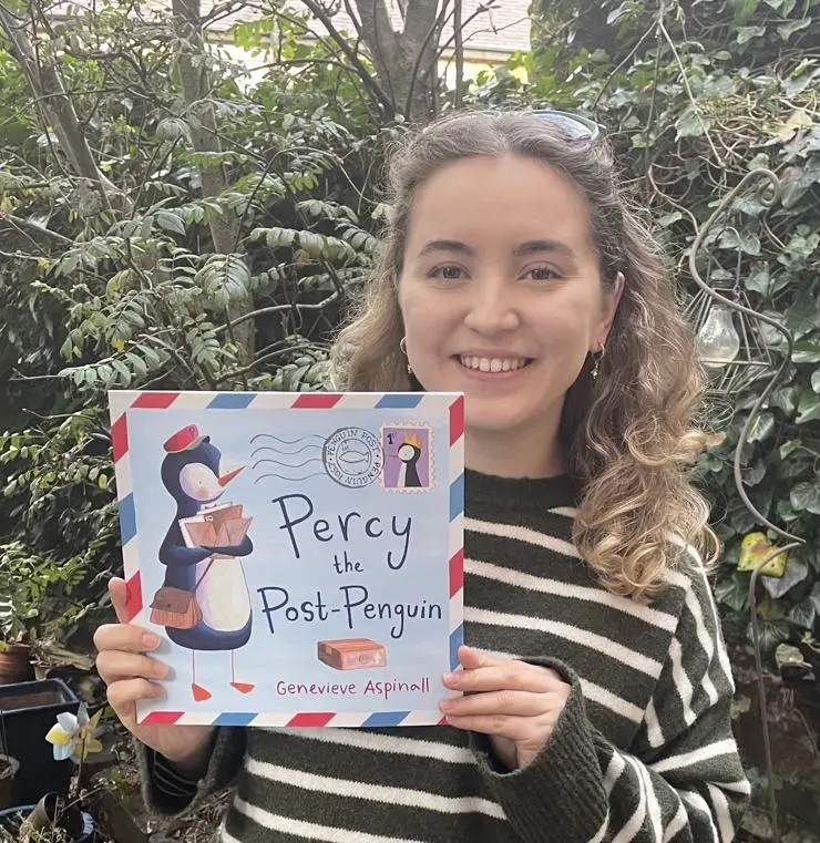 BA (Hons) Illustration and MA Children’s Book Illustration Alumna Genevieve Aspinall holding her book 'Percy the Post-Penguin'