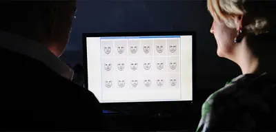Two people looking at a computer featuring computer generated faces.