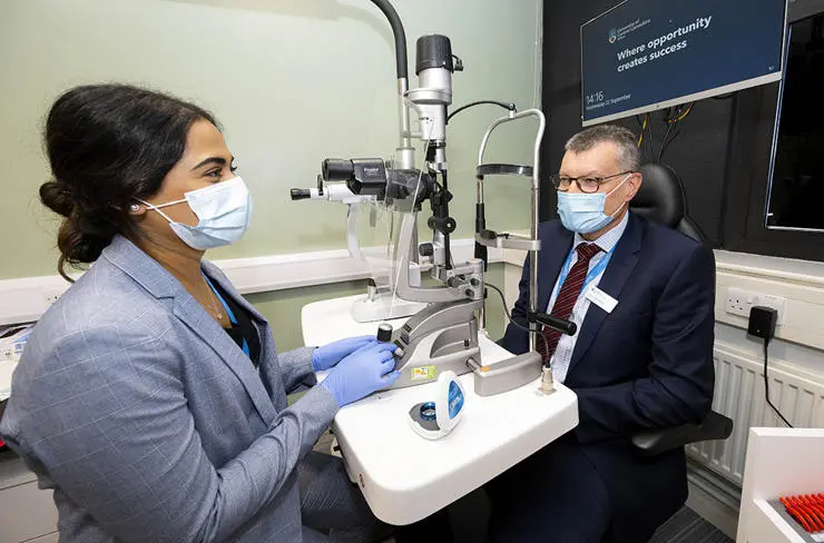 Hafsa Patel, Eye Health Clinic Manager with UCLan Vice-Chancellor Professor Graham Baldwin. Hafsa is about to use a Slit Lamp, a microscope which allows to the clinician to assess the front of the eye is more detail.