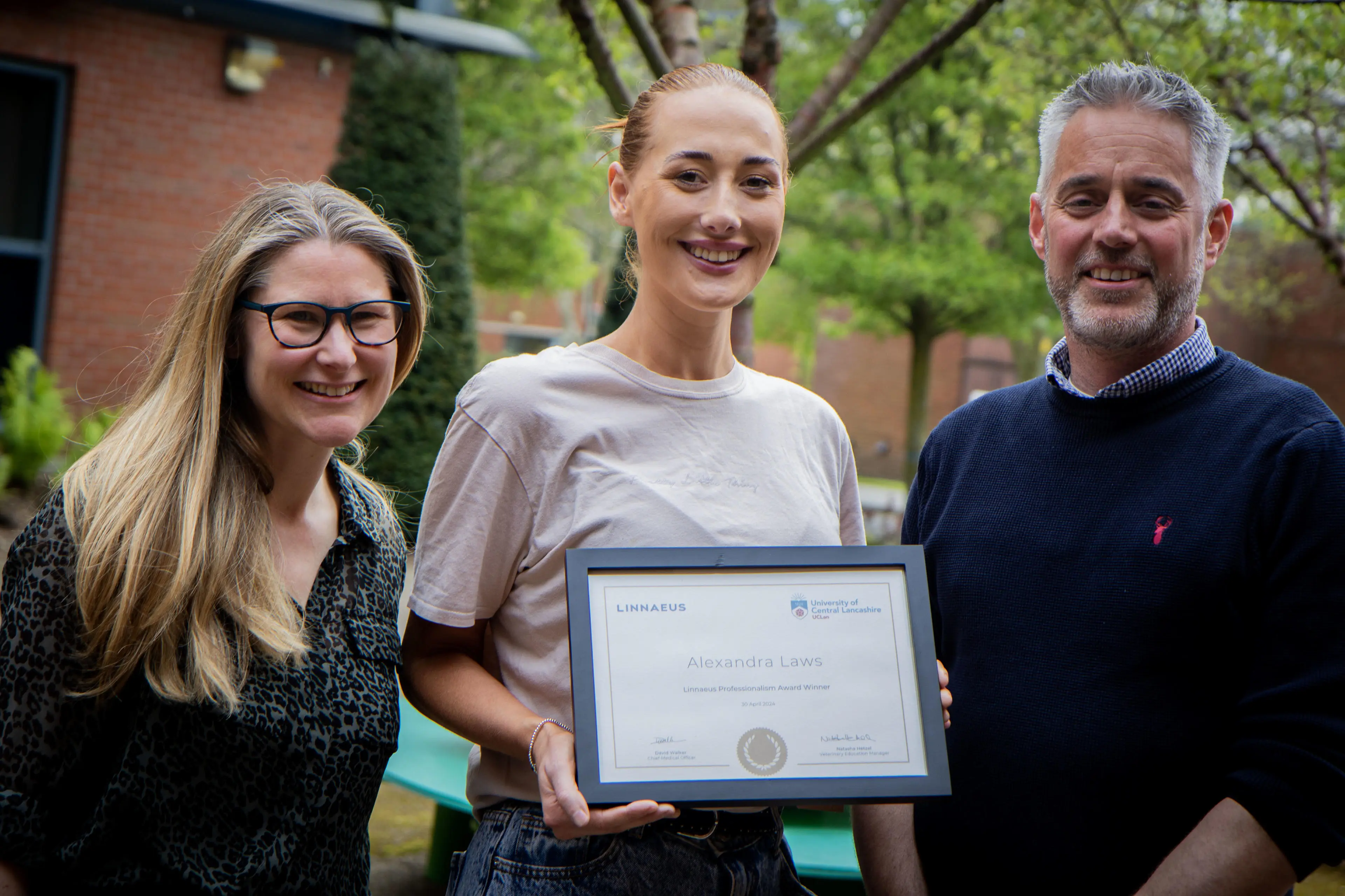 Three people stood together with one holding a framed certificate
