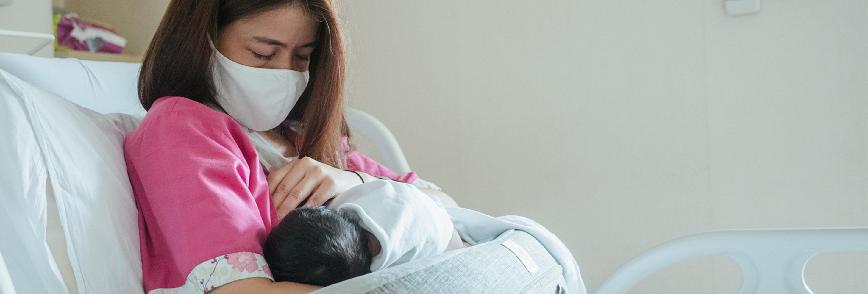 Woman in hospital bed wearing a mask and holding a newborn baby