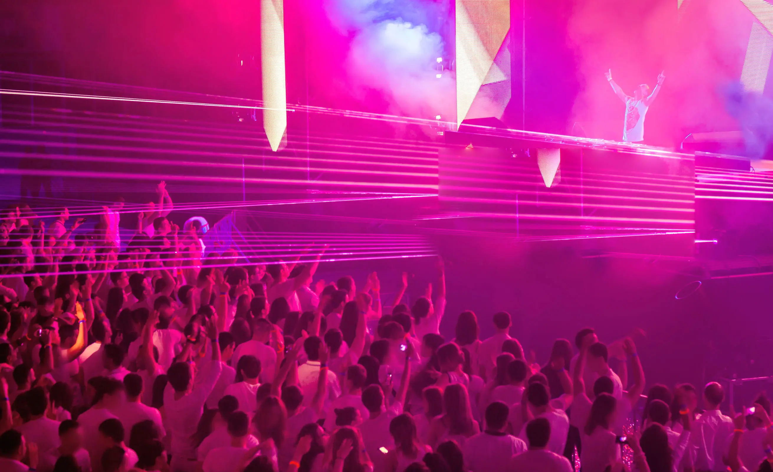 A DJ on stage with a big crowd of people and pink lights shining on the audience