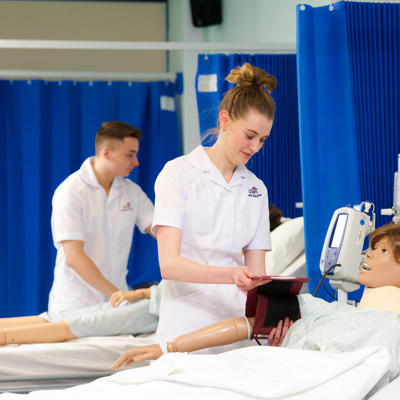 Two student nurses training with medical dummies.