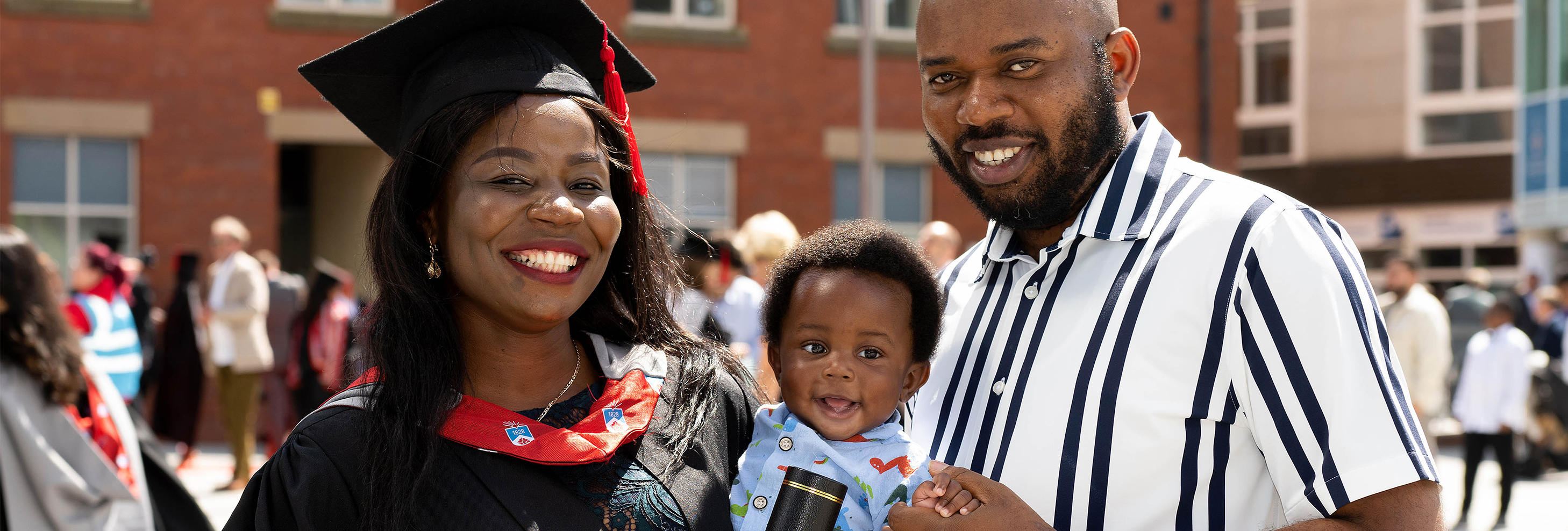 A woman in academic gowns holding a baby boy with a man next to her