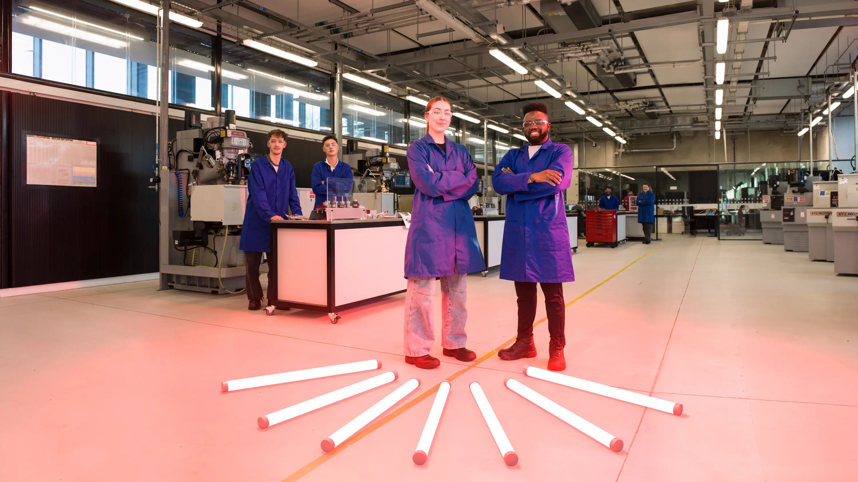 four students in an engineering lab with 7 neon rods on the floor illuminating them