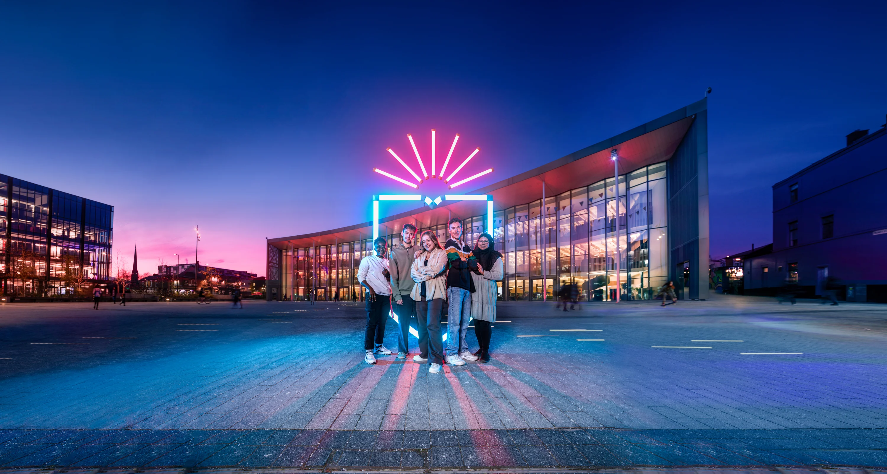 group of students stood in front a neon UCLan logo in front of the student centre
