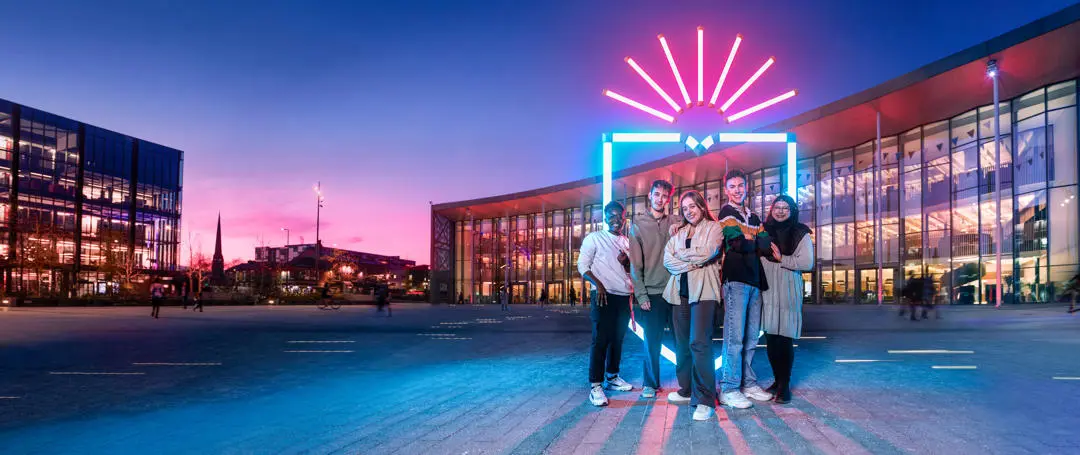 group of students stood in front a neon UCLan logo in front of the student centre
